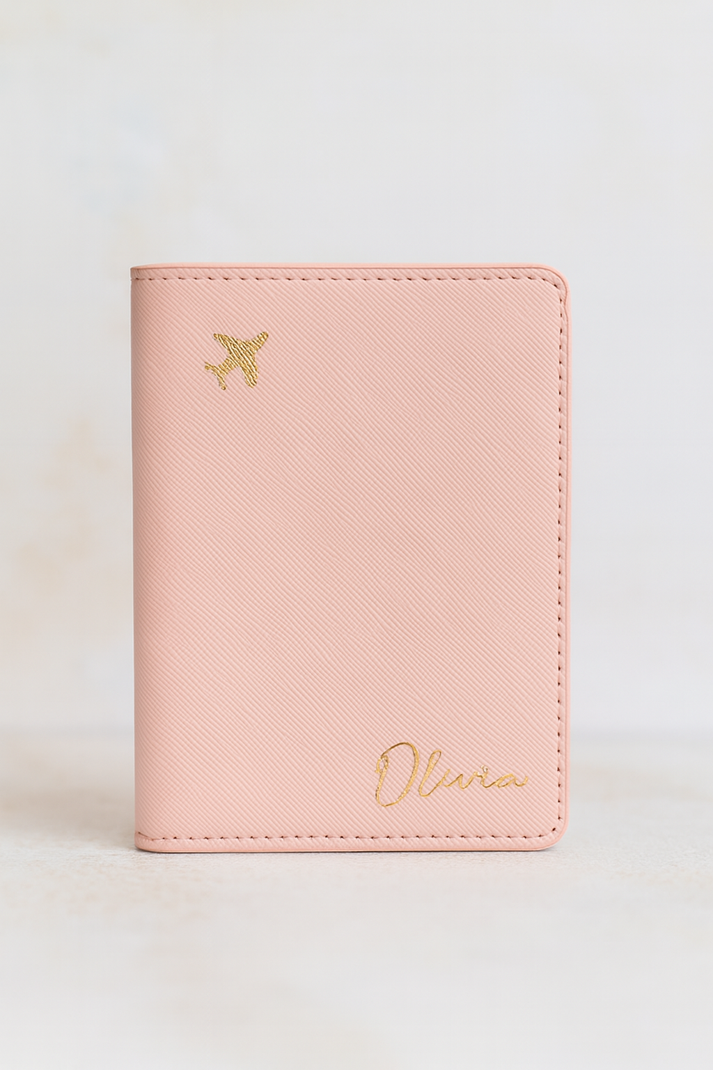 Pink passport holder with gold airplane and name on a light beige background