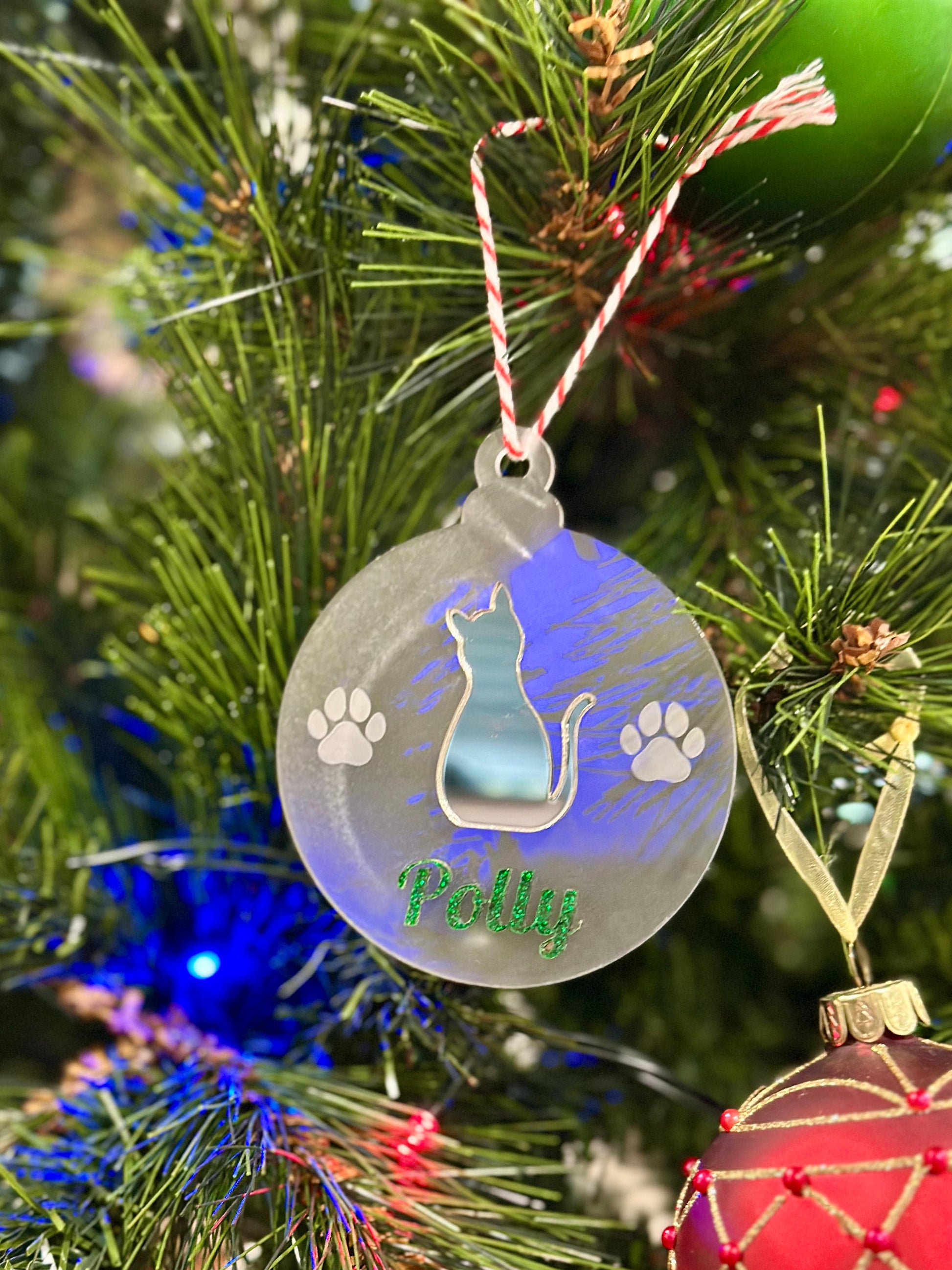 Decorative Christmas ornament with a cat design and 'Polly' text, hanging on a tree.