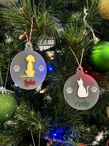 Two Christmas ornaments with dog and cat silhouettes on a decorated tree.
