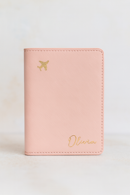 Pink passport holder with gold airplane and name on a light beige background